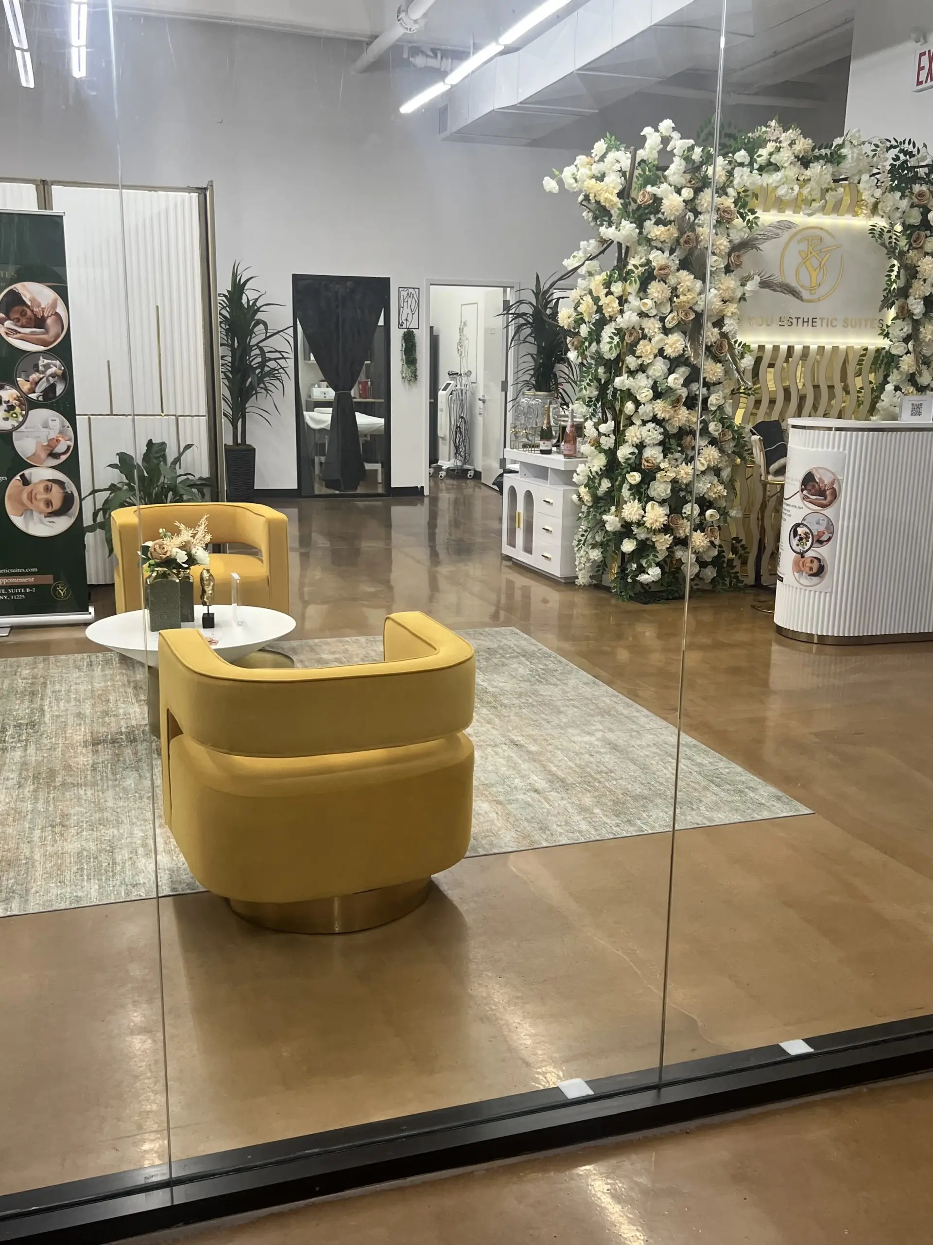 Interior view of Be You Esthetic Suites featuring yellow seating, decorative floral wall, and treatment area.