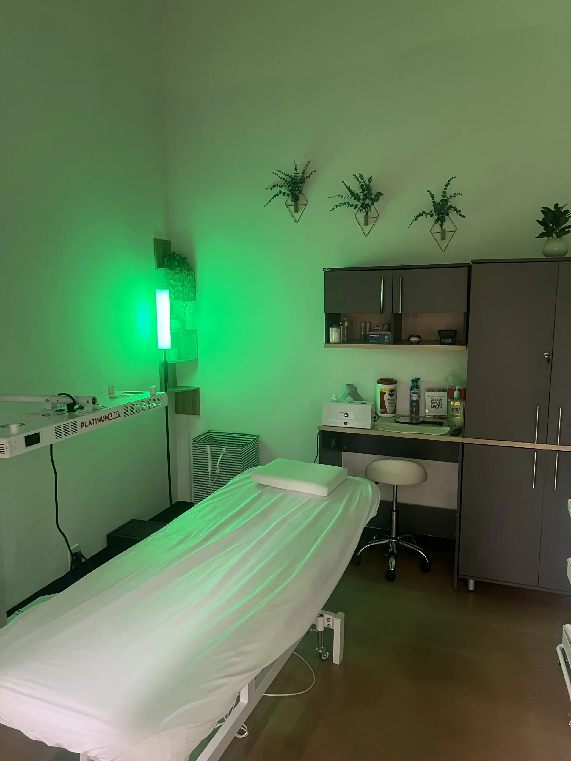 Private esthetic suite interior featuring a treatment bed, green ambient lighting, and storage for skincare products.