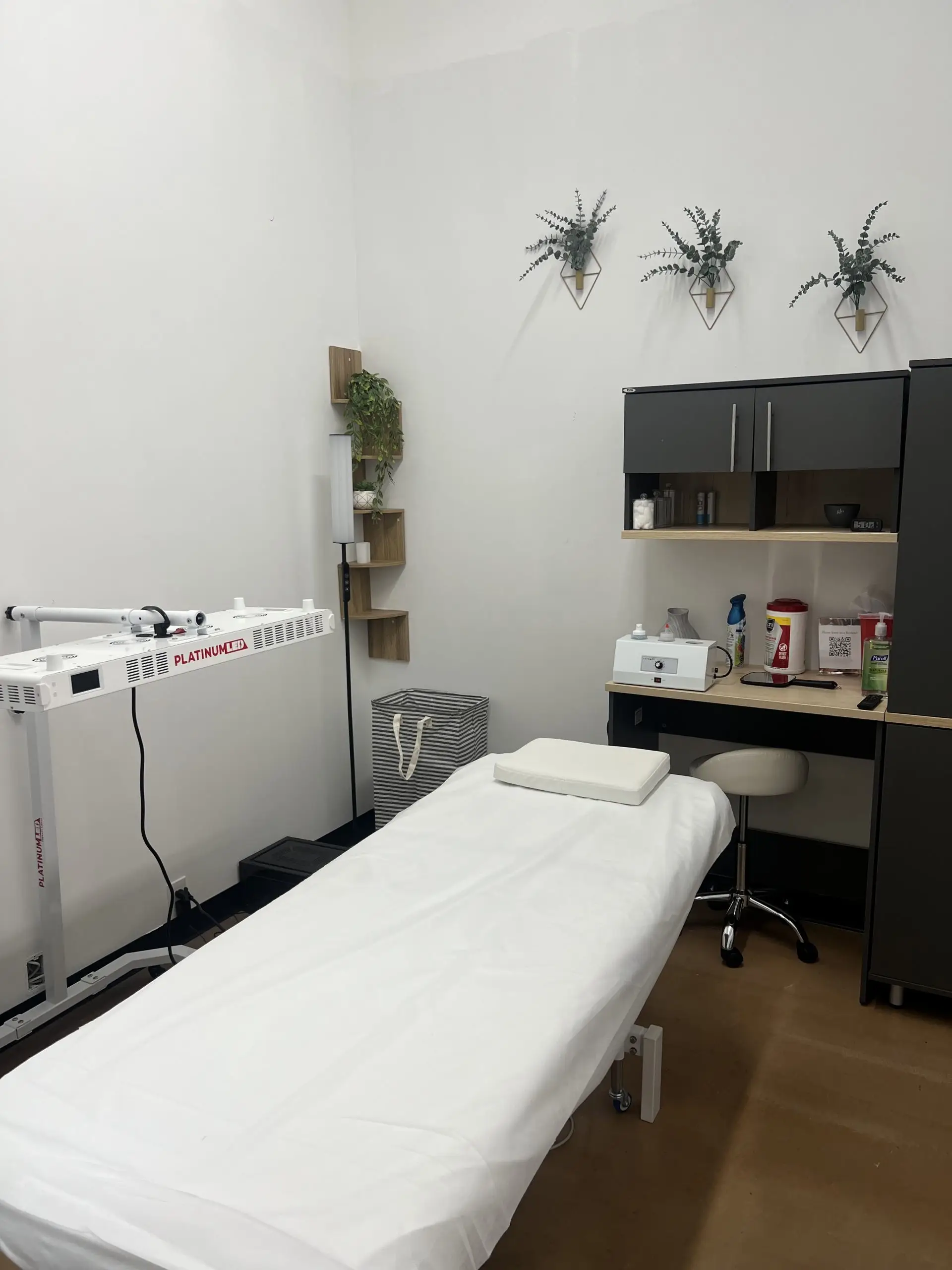 Private esthetic suite with treatment bed, LED therapy light, and organized storage.
